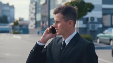 Klasik takım elbiseli, telefonla konuşan ve sokakta yürüyen kendine güvenen bir iş adamının portresi. Genç iş adamı iş görüşmesi yapıyor..