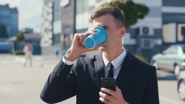 Retrato de Jovem Empresário Atraente usando seu Smartphone e Beber Café. Perto do edifício de escritórios moderno. Vestindo terno clássico. Rede Social — Vídeo de Stock