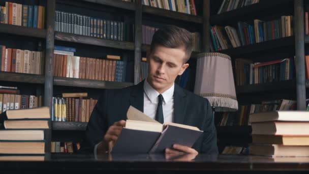 Biznesmen w klasycznym garniturze siedzi w bibliotece i czyta książki. — Wideo stockowe