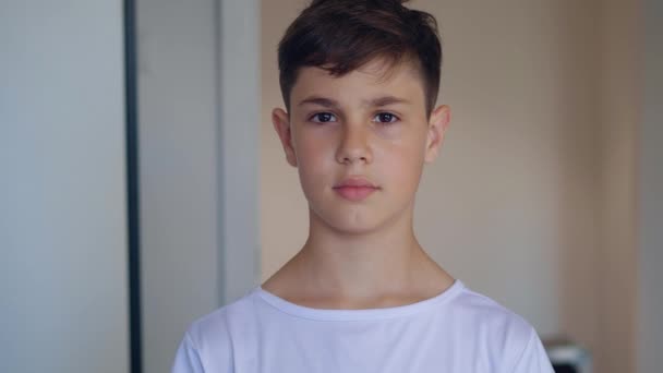 Portrét pohledného chlapce 11 let v bílém tričku při pohledu na kameru doma — Stock video