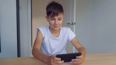 Mutlu çocuk evde akıllı telefondan cep telefonu oyunu oynuyor. Anaokulu öğrencisi cep telefonu çalıyor. Çocuk oyun oynamak için telefonu kullanıyor. Video oyunu oynayan çocuk.