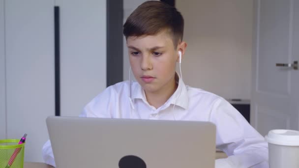 Schoolboy in headphones using laptop computer for online education at home. Kid enjoys making school homework online. Young boy businessman working laptop and drinking coffee — Stock Video