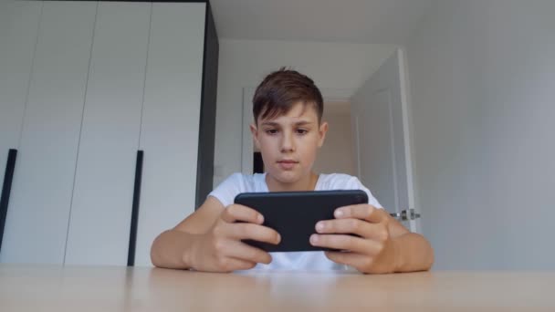 Jongen speelt mobiel spel op smartphone thuis. Een kleuter die mobiele telefoon speelt. Hij gebruikt telefoon om te gamen. Kind spelen video game. — Stockvideo