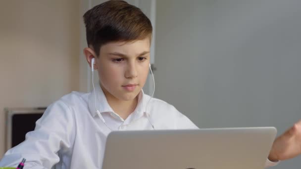 Schoolboy em fones de ouvido usando computador portátil para educação on-line em casa. O miúdo gosta de fazer trabalhos de casa online. Jovem homem de negócios trabalhando laptop e beber café — Vídeo de Stock