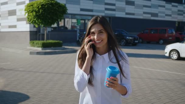 Güzel, şık bir kadının portresi telefonda konuşmaktan ve şehirde yürürken kahve içmekten zevk alıyor. Gülümseyen iş kadını — Stok video