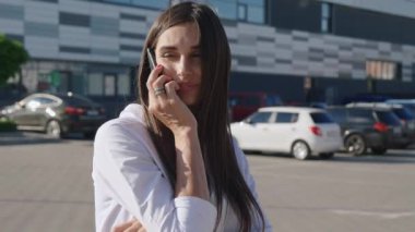 Beyaz Gömlekli Gülümseyen Genç İş Kadını Modern Ofis Binası 'nın önünde telefonda konuşuyor. Uzun Saçlı Çekici Kadın Şehir Caddesinde Dışarda Dururken Cep Telefonuyla Konuşuyor.