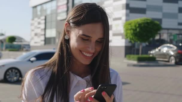 Улыбающаяся деловая женщина с помощью смартфона в центре города. Привлекательная молодая женщина наслаждается использованием телефона для социальных сетей на открытом воздухе . — стоковое видео