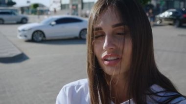 Şehrin arka planında kameraya bakan gülümseyen güzel bir kadın. Genç iş kadını şehirde ağır çekimde başarılı bir yaşam tarzının tadını çıkarıyor. Sabit çekim.