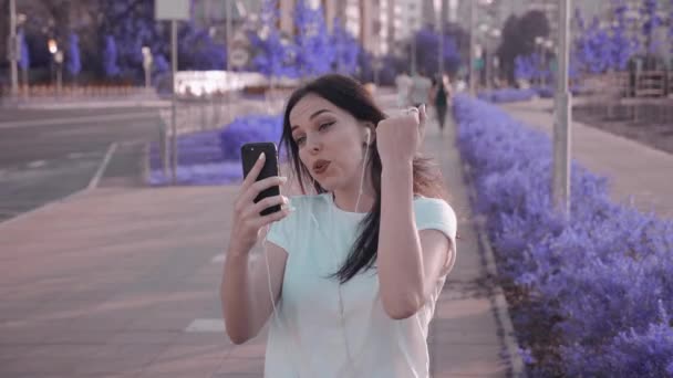 Mujer joven despreocupada disfrutando de su música favorita por los auriculares, bailando y caminando por la calle en el fondo urbano de la ciudad . — Vídeos de Stock