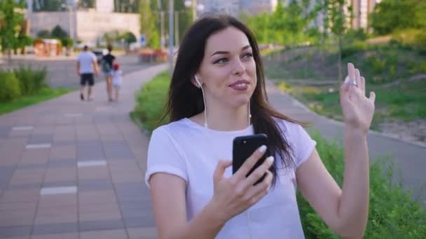 Νεαρή γυναίκα που χρησιμοποιεί το κινητό της τηλέφωνο κατά τη διάρκεια διαδικτυακής βιντεοκλήσης ενώ περπατάει στην πόλη — Αρχείο Βίντεο