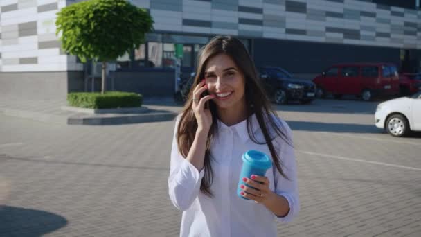 Портрет красивої стильної жінки, яка насолоджується розмовою по телефону і питною кавою, щоб піти під час прогулянки по місту. Усміхнена бізнес-леді — стокове відео