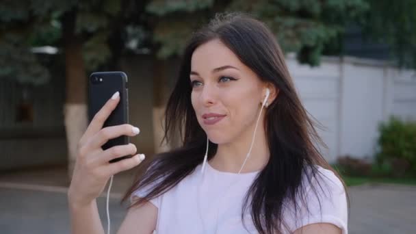 Молодая женщина использует свой мобильный телефон во время онлайн видео-звонка во время прогулки по городу — стоковое видео