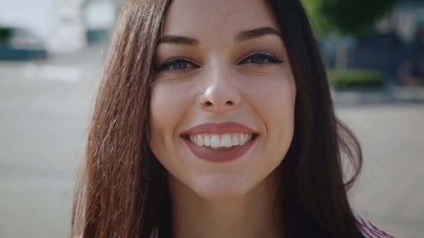 Πορτρέτο μιας χαρούμενης ανέμελης γυναίκας χαμογελώντας μπροστά από το φόντο της πόλης, Γκρο πλαν πρόσωπο της νεαρής γυναίκας χαμογελώντας με τα δόντια σε εξωτερικούς χώρους. — Αρχείο Βίντεο
