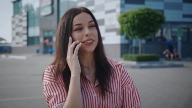 Telefonda konuşan mutlu genç bir kadın. Modern ofis binasının yanında. Akıllı telefon kullanan bir iş kadını. Dışarıda telefonla konuşan gülümseyen kız..