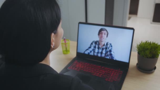 Close-up joven mujer hace una videollamada de conferencia en el ordenador portátil y bebe café. Mujer de negocios viendo webinar en línea utilizando la llamada de conferencia web portátil en casa. Vista de pantalla portátil sobre hombro . — Vídeos de Stock