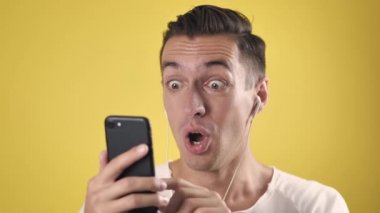 Heyecanlı erkek kazananın akıllı telefonu var. İnternet üzerinden bahis uygulamasının sarı arka planda kazanması, mutlu erkek kullanıcısının cep telefonuna bakması, iyi haberleri okuması karşısında şaşkına dönüyor.