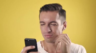 Kulaklıklı neşeli adam sarı arka plandaki akıllı telefondan en sevdiği şarkıları dinliyor..