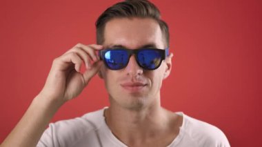 Heyecanlı adam stüdyoda başarıyı kutluyor. Mutlu insan portresi güneş gözlüğü fırlatır ve evet işareti gösterir. Kırmızı arka planda el ele tutuşan neşeli erkek. Mutlu adam ağır çekimde gülümsüyor.