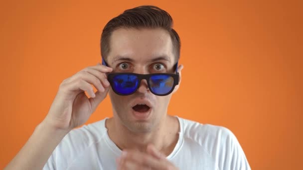 Stijlvolle jongeman geschokt en verrast op oranje achtergrond. Man hipster in verrassing schiet zonnebril en kijkt naar de camera in verrassing. — Stockvideo