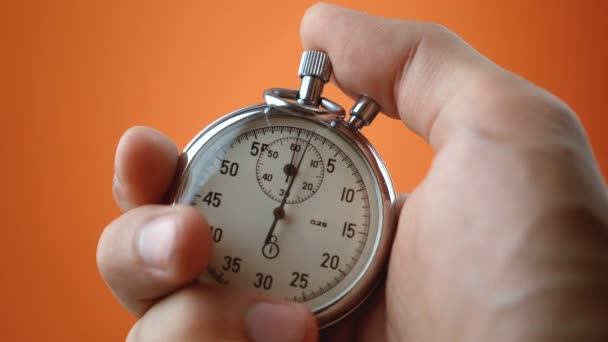 Mannelijke hand met analoge stopwatch op oranje achtergrond. Tijd start met oude chronometer man drukt op start knop in de sport concept. Tijdbeheerconcept. — Stockvideo