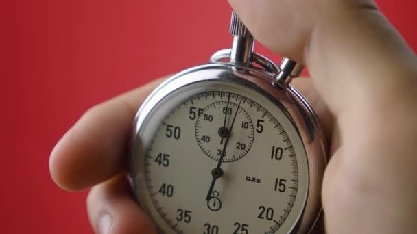 Close-up analog stopwatch in mans hand on red background is starting and stopping — Stock Video