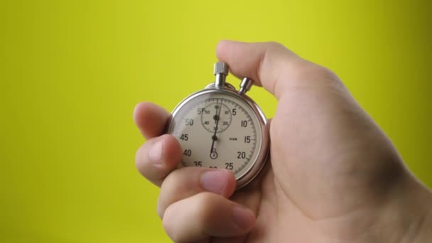 Man hand hålla analogt stoppur på gul bakgrund. Tiden börjar med gamla kronometer man trycker på startknappen i sport konceptet. Tidsplanering. — Stockvideo