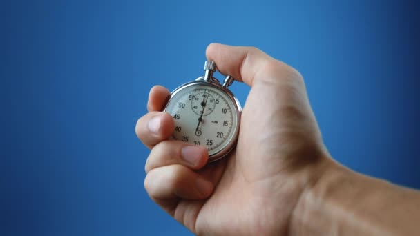 Man hand hålla analogt stoppur på blå färg bakgrund. Tiden börjar med gamla kronometer man trycker på startknappen i sport konceptet. Tidsplanering. — Stockvideo