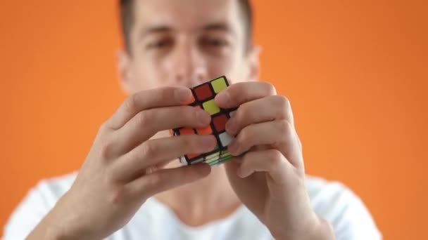 Kiev, Ukraina, 30 juli 2020: Rubiks kub i händerna på en man i studio på orange färg bakgrund, närbild — Stockvideo