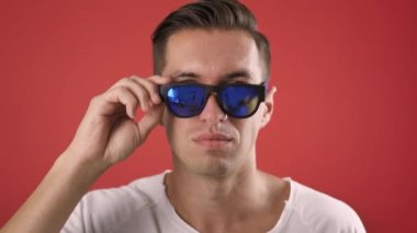 Tarz sahibi genç adam kırmızı arka plana şaşırmış ve şaşırmıştı. Şaşkınlık içindeki hippi adam güneş gözlüğü kullanır ve kameraya ağır çekimde şaşırarak bakar.