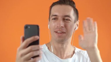 Günlük giysiler içinde mutlu bir adamın portresi. Stüdyodaki akıllı telefonuyla görüntülü konuşma yapıyor. Konferans toplantısını online uygulama, sosyal uzaklık kullanarak