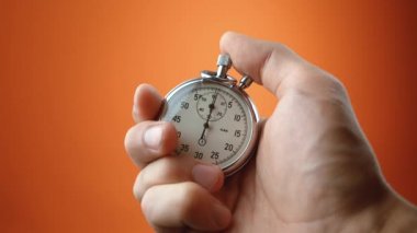 Turuncu arka planda analog kronometre tutan bir erkek. Zaman, spor konseptindeki eski kronometre adam başlatma düğmelerine basarak başlar. Zaman yönetimi kavramı.