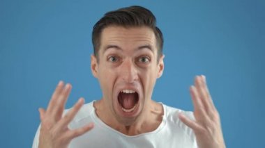 Genç adam zafer için sevinçten bağırıyor. Kazanan genç erkek mavi arka planda evet işareti gösteriyor..