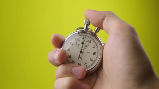 Mannelijke hand met analoge stopwatch op gele achtergrond. Tijd start met oude chronometer man drukt op start knop in de sport concept. Tijdbeheerconcept. — Stockvideo
