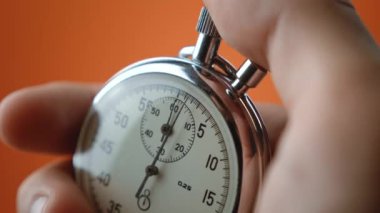 Turuncu arka planda analog kronometre tutan bir erkek. Zaman, spor konseptindeki eski kronometre adam başlatma düğmelerine basarak başlar. Zaman yönetimi kavramı.