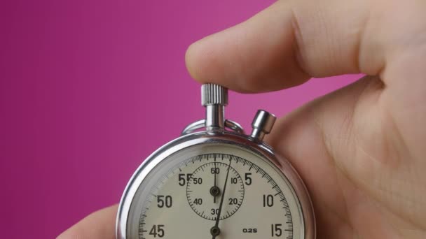 Gros plan chronomètre analogique en mans main sur fond rose commence et s'arrête — Video