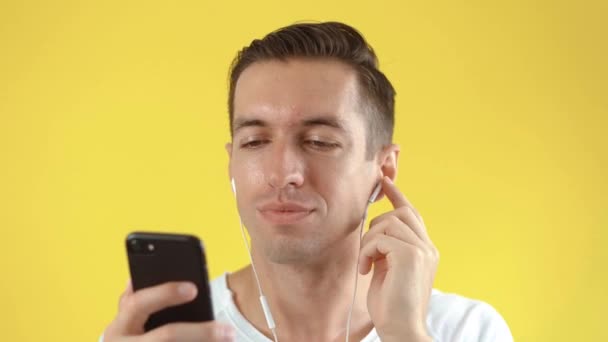 Fiatal hipster férfi napszemüveg élvezi hallgatni a zenét a fülhallgató segítségével okostelefon sárga színű háttér — Stock videók