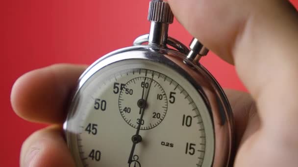 Mão masculina segurando cronômetro analógico no fundo vermelho. O tempo começa com o velho cronômetro homem pressiona botão iniciar no conceito de esporte. Conceito de gestão do tempo . — Vídeo de Stock