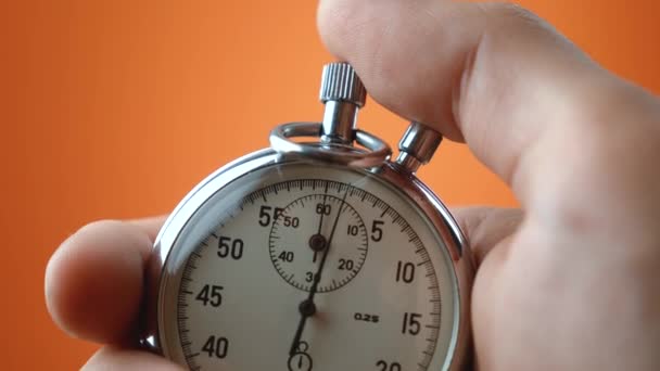 Reloj de mano masculino con cronómetro analógico sobre fondo de color naranja. El tiempo comienza con el viejo cronómetro hombre presiona el botón de inicio en el concepto de deporte. Concepto de gestión del tiempo. — Vídeo de stock