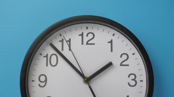Close-up pojedynczy biały zegar biurowy wiszący na niebieskim kolorze ściany. — Wideo stockowe