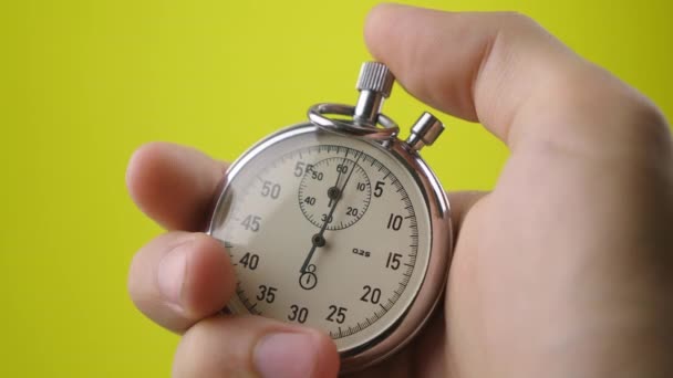 Close-up analog stopwatch in mans hand on yellow background is starting and stopwatch — Stok Video
