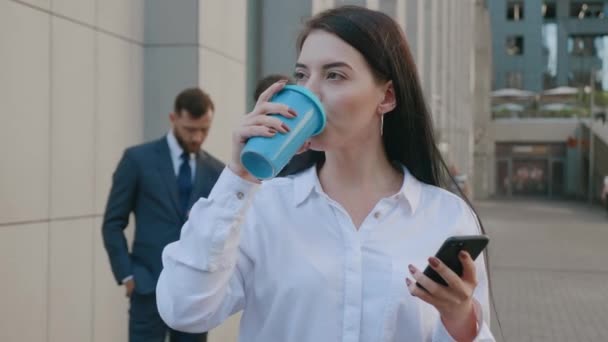Portrait de belle jeune femme d'affaires utilisant smartphone sur pause café à l'extérieur dans les rues du quartier des affaires. Groupe de gens d'affaires occupés sur le fond. — Video