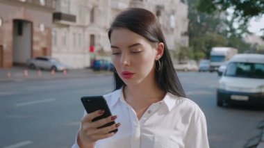 Şehrin arka planında akıllı telefon kullanan çekici genç bir kadın..