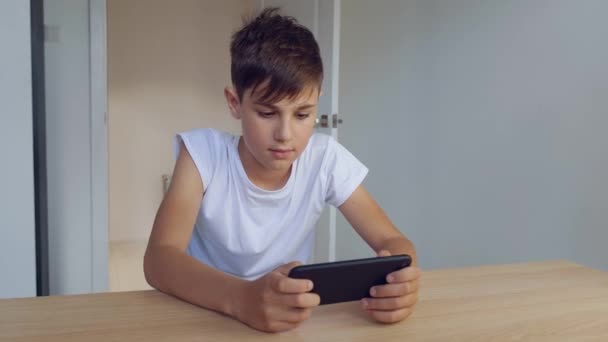 Menino jogando jogo móvel no smartphone em casa. Pré-escolar a jogar telemóvel. Miúdo a usar o telefone para jogar. Criança jogando videogame. — Vídeo de Stock