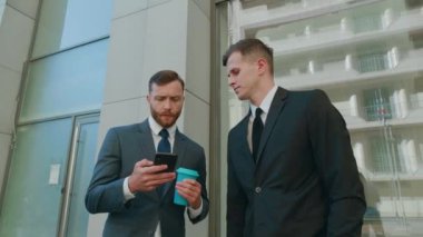 Şehir merkezindeki iş bölgesinde birbiriyle etkileşim halinde olan iki erkek çalışan. Akıllı telefon kullanan kendine güvenen işadamları şirket çalışmasında bilgisayar projesi planlamayı tartışıyorlar.