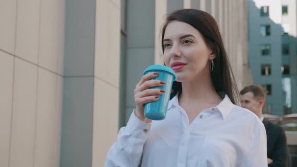 Retrato de una mujer de negocios sonriente con taza de café al aire libre cerca del moderno edificio de oficinas. Hermosa empleada morena sonriendo a la cámara en el fondo del centro de la ciudad — Vídeo de stock