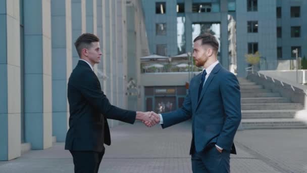 Twee zakenpartners schudden elkaar de hand. Portret van een handdruk van twee succesvolle zakenmannen die een deal maken. Kantoorgebouw op de achtergrond. Bedrijfsdistrict. — Stockvideo