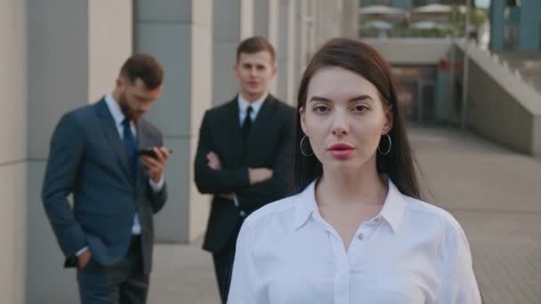 Portrait d'une jeune femme d'affaires prospère à l'extérieur près d'un immeuble de bureaux moderne. Belle employée brune regardant sérieusement la caméra sur fond de gens d'affaires. Classique habillé. — Video