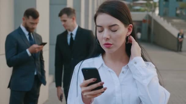 ビジネス街の路上でコーヒーブレイクの屋外でスマートフォンを使用して美しい若い女性ビジネスマンの肖像画。バックグラウンドで忙しいビジネスの人々のグループ. — ストック動画