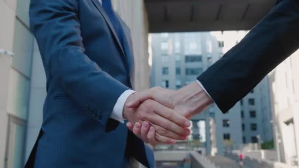 Закрыть руки топ-менеджерам в деловых костюмах, пожать друг другу руки, на фоне бизнес-центра, согласиться на сделку или поздороваться. Неузнаваемый человек с медленным движением — стоковое видео