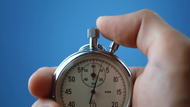 Man hand hålla analogt stoppur på blå färg bakgrund. Tiden börjar med gamla kronometer man trycker på startknappen i sport konceptet. Tidsplanering. — Stockvideo